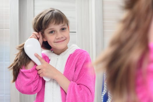Happy girl combing hair in the bathroom