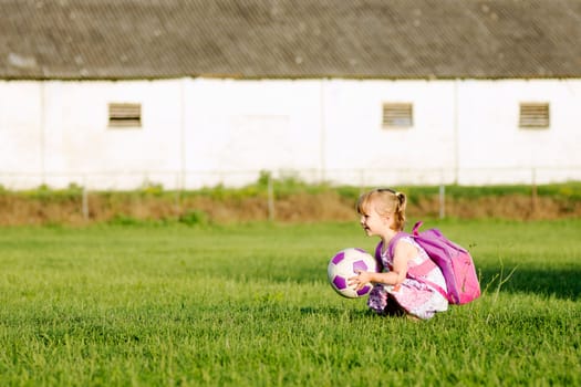 The playful blonde little girl in pink is playing with soccer ball on grass outdoors.