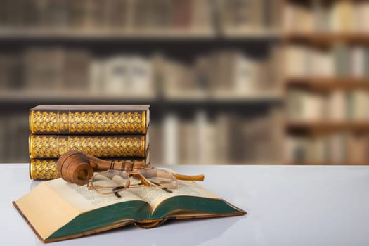 Closeup of an old book with a tobacco pipe and a reading glasses on on it with further books on a bright table in front of a blurred bookshelf in library. Education concept.