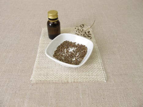 Essential dill oil in a bottle and dill seeds in a bowl