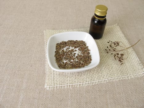 Essential dill oil in a bottle and dill seeds in a bowl