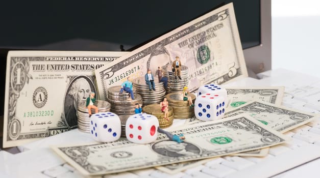 Online gambling concept with miniature people and coins on top of a notebook