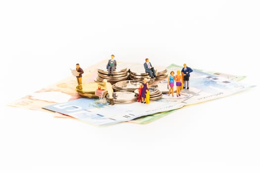 Miniature people and coins on top of banknotes