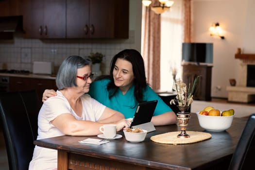 Caring nurse showing a digital tablet to an elderly woman in a nursing home. Spending time together.