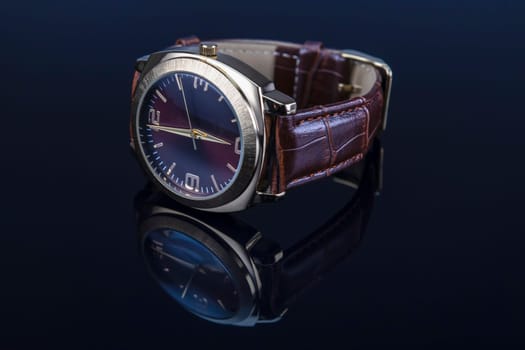 Men wrist watch with leather bracelet on black glossy background.