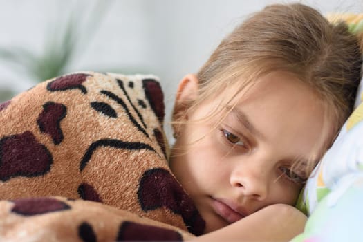 Girl slowly wakes up, lying in bed and covered with an old blanket
