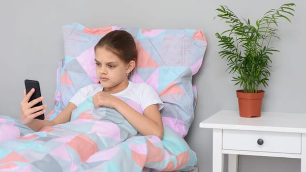 Girl communicates by video calling while lying in bed with a mobile phone