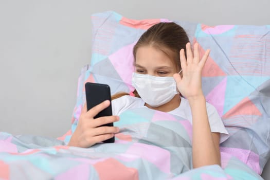 A sick girl lies in bed and communicates with friends online via video-telephone