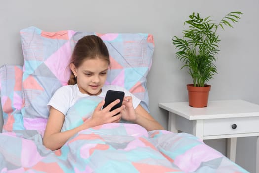 Girl communicates with friends online in a mobile phone while lying in bed.