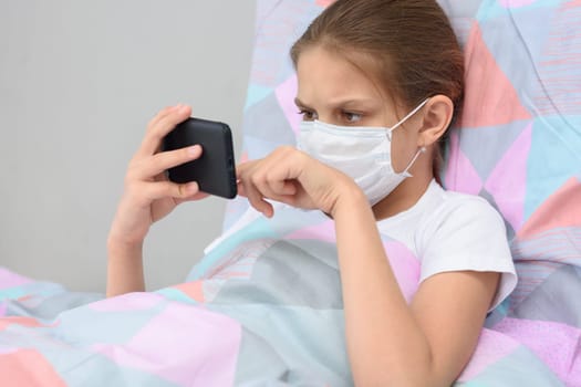 The quarantined girl lies in bed with a mobile phone