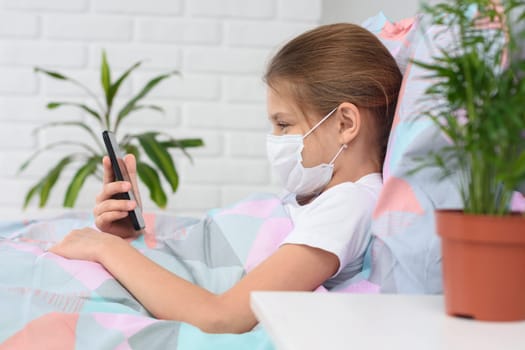 A girl in a hospital ward lies on a bed in a medical mask and does web surfing on the phone