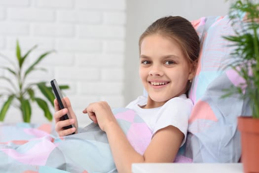 The girl plays in the mobile phone and looked happily into the frame.