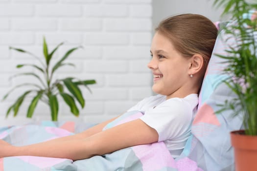 Happy ten-year-old girl in the morning lies in bed and smiles