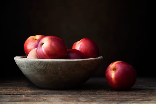Nectarines in wooden bowl on dark wooden table.