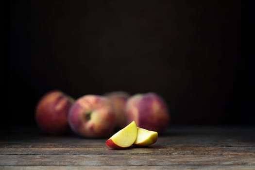 Fresh nectarines, whole and sliced, on  a rustic wooden table with a dark background