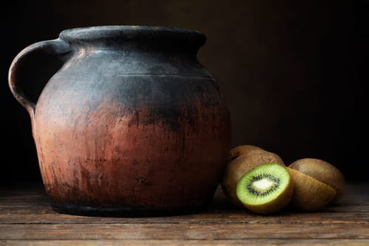 Fresh kiwi, both whole and sliced, on wooden table with rustic pottery jug