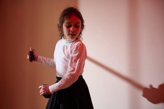 A young girl performs a dance move illuminated by warm colored lighting, creating a contrast between shadow and light, emphasizing expressive motion and emotion.