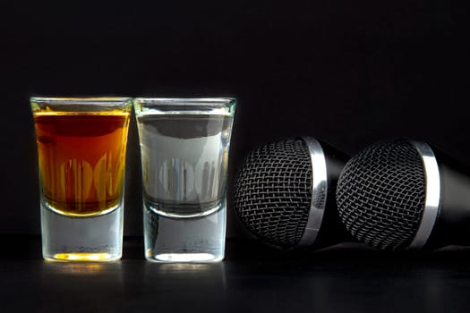 Shoot Glasses with liquor and two karaoke microphones on a black background