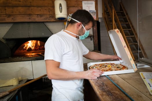 Man is working in a pizza restaurant drive with his mask and covid 19 protection. Pandemic situation