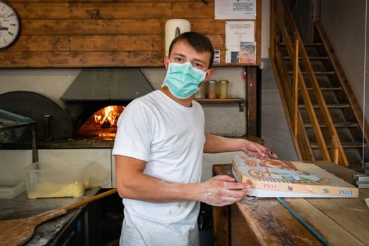 Man is working in a pizza restaurant drive with his mask and covid 19 protection. Pandemic situation