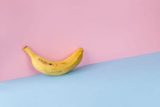 Minimalist image of a banana on a light blue and pink background. Copy space available.