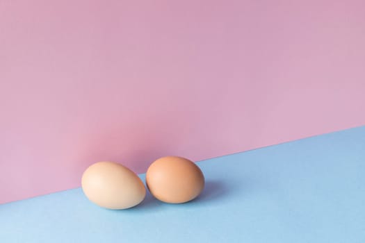 Minimalist image of two brown eggs on a light blue and pink background. Copy space available.