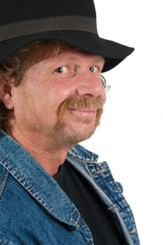 Cropped side head and shoulder portrait of an older man with a black hat and blue jeans jacket mischievously smiling at the camera isolated on white.