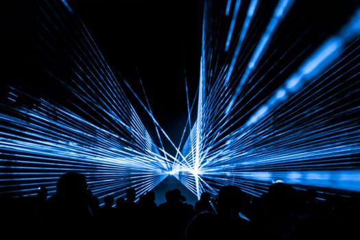 Luxury entertainment with audience silhouettes in nightclub event, festival or New Year's Eve. Beams and rays shining colorful lights.
