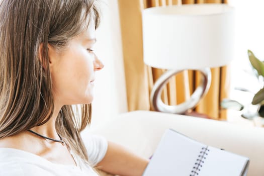 Mature woman sitting on a couch and is checking notes in her notebook