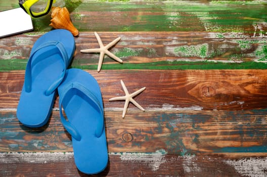 Flat lay summer beach accessories of blue flip flops , smartphone, snorkel with seashell and starfish on wooden background. Summer vacation and travel concept.