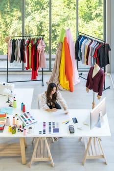 Top view of young adult asian fashion designer drawing and sketching her work at home as atelier studio with colour palette. Using for entrepreneur small business startup concept.