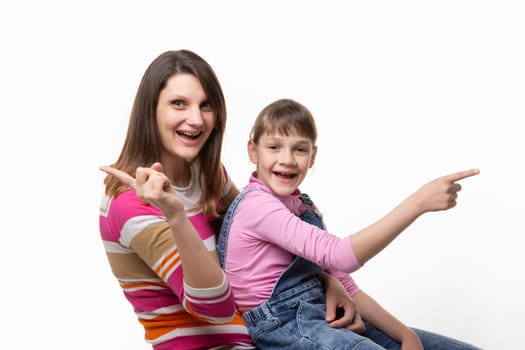 Joyful mom and daughter point finger in different directions, isolated on white background