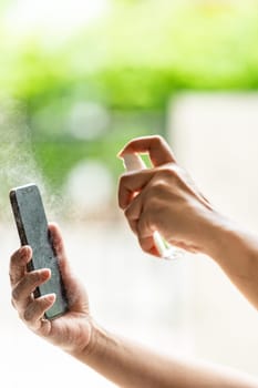 close-up cleaning mobile phone using alocohol spray from bottle spraying, disinfection for safety prevent and protect from infection of virus and germ Covid-19 coronavirus world pandemic.