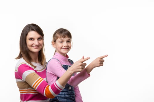 A girl sits on her mothers lap and joyfully points a finger at an empty place, looks into the frame