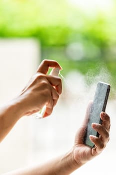close-up cleaning mobile phone using alocohol spray from bottle spraying, disinfection for safety prevent and protect from infection of virus and germ Covid-19 coronavirus world pandemic.