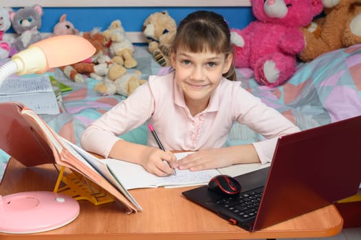 A child learns at home at a desk with toys in the background