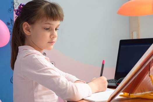 Girl does a job from a textbook at home sitting at a table