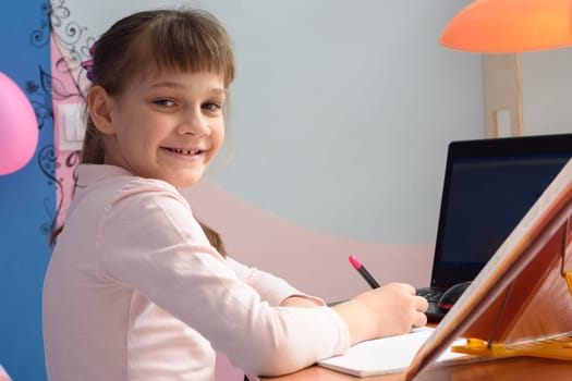 Girl in good spirits doing homework at the desk at home