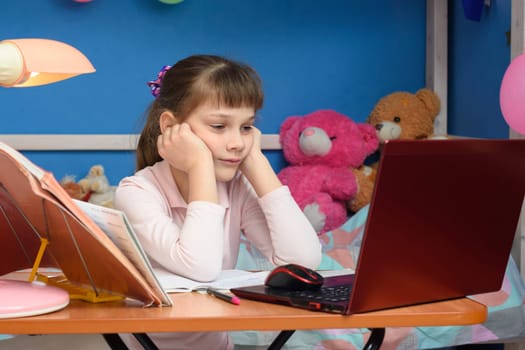 brooding girl sits in front of a laptop with her hands in her head in the children's room