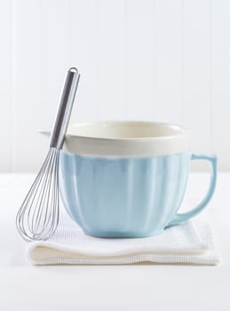 Blue mixing bowl with wisp for baking on white background. Kitchen utensil for cooking and baking.