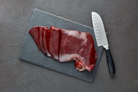 Raw beef livers on a black stone cutting board  on dark background. Top view