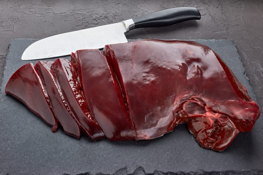 Raw beef livers on a black stone cutting board  on dark background. Top view