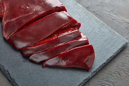 Raw beef livers on a black stone cutting board  on dark background. Top view