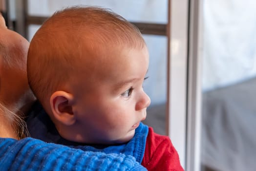 Cute 6 months little baby boy with curiosity expression on his face in his mothers arms