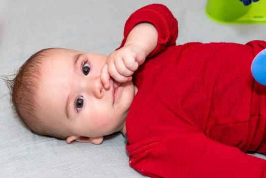 Adorable 6 months old little baby boy on his back surrounded by colourful toys