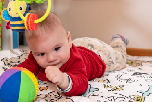 Adorable 6 months old little baby boy during tummy time surrounded by colourful toys