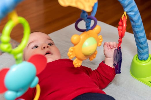 Adorable 6 months old little baby boy on his back surrounded by colourful toys