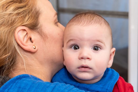 Cute 6 months little baby boy with curiosity expression on his face in his mothers arms