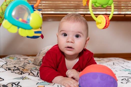 Adorable 6 months old little baby boy during tummy time surrounded by colourful toys