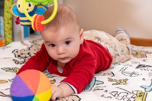 Adorable 6 months old little baby boy during tummy time surrounded by colourful toys